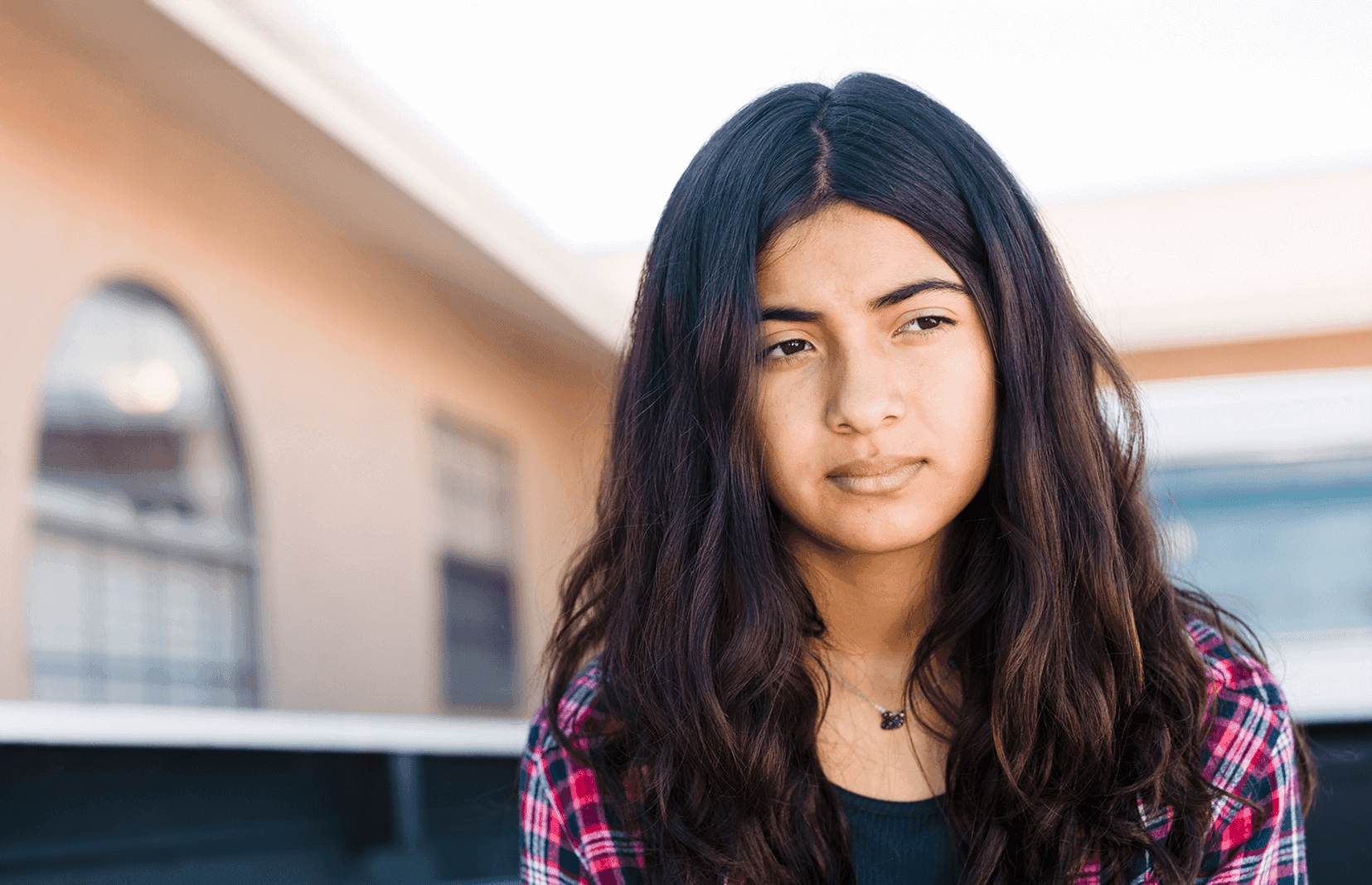Teen girl with dark hair and dark features, somberly looking into the distance.